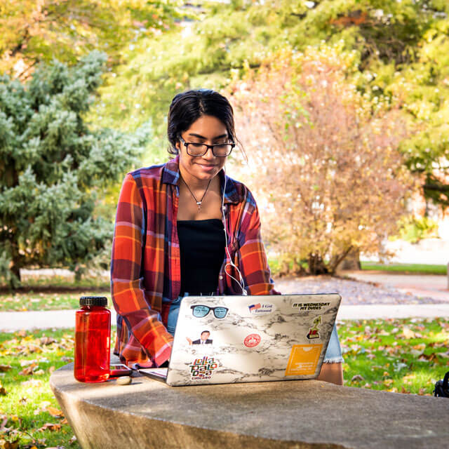Student uses a laptop on a bench on the quad.